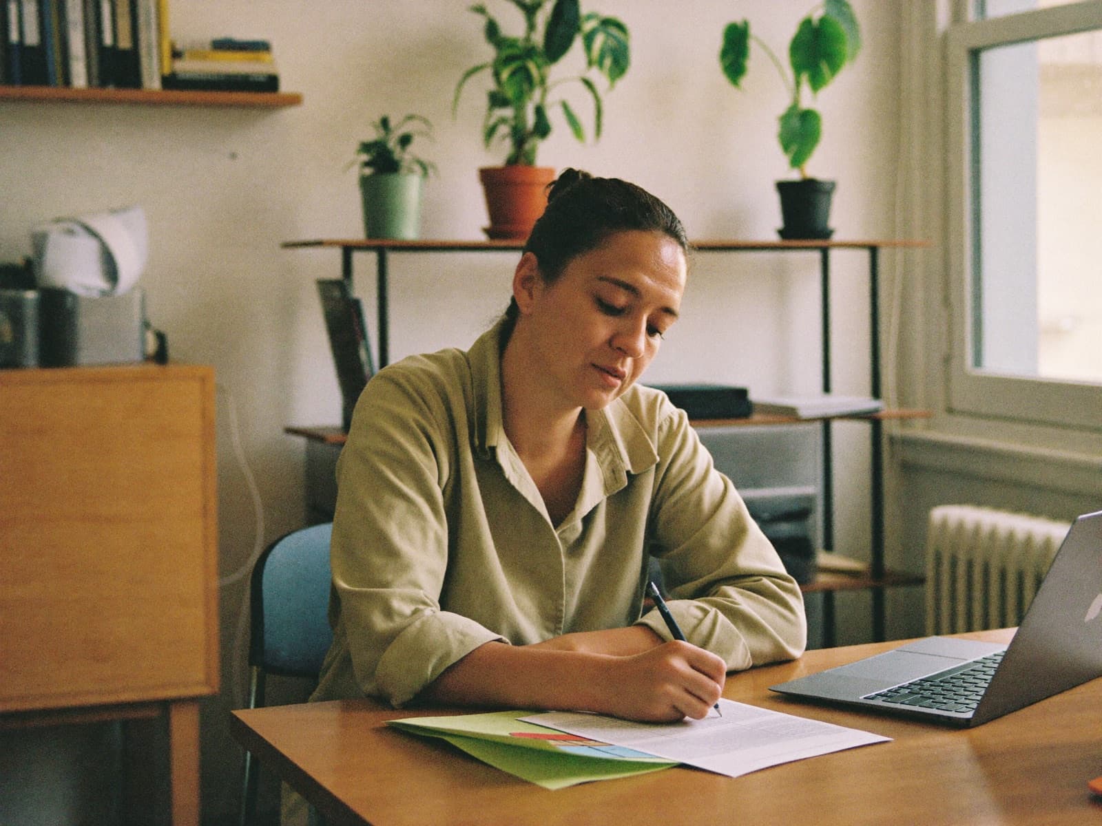 A director drafting notes beside a laptop at a sunlit office desk.