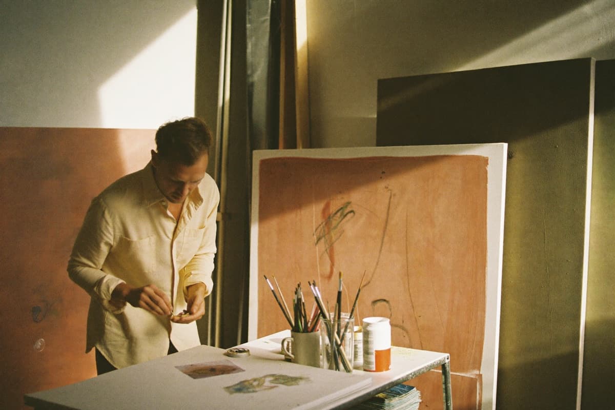 An artist working in a sunlit studio among canvases in progress.